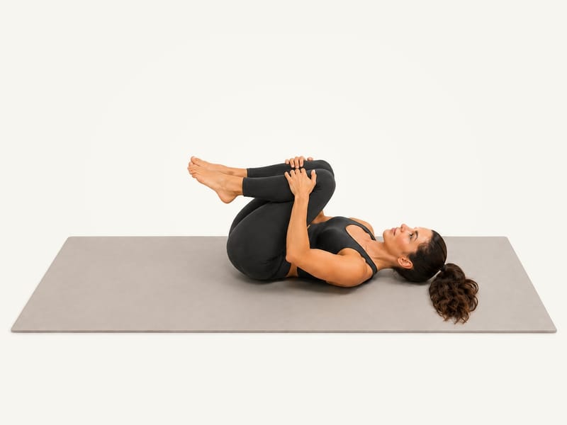 Happy baby pose set-up: lying on the back with both knees drawn towards the chest, hands on the shins