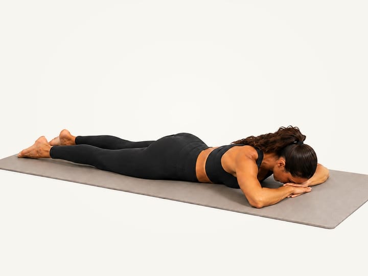 Step 1 of sphinx pose: lying face down with the forehead resting on the hands